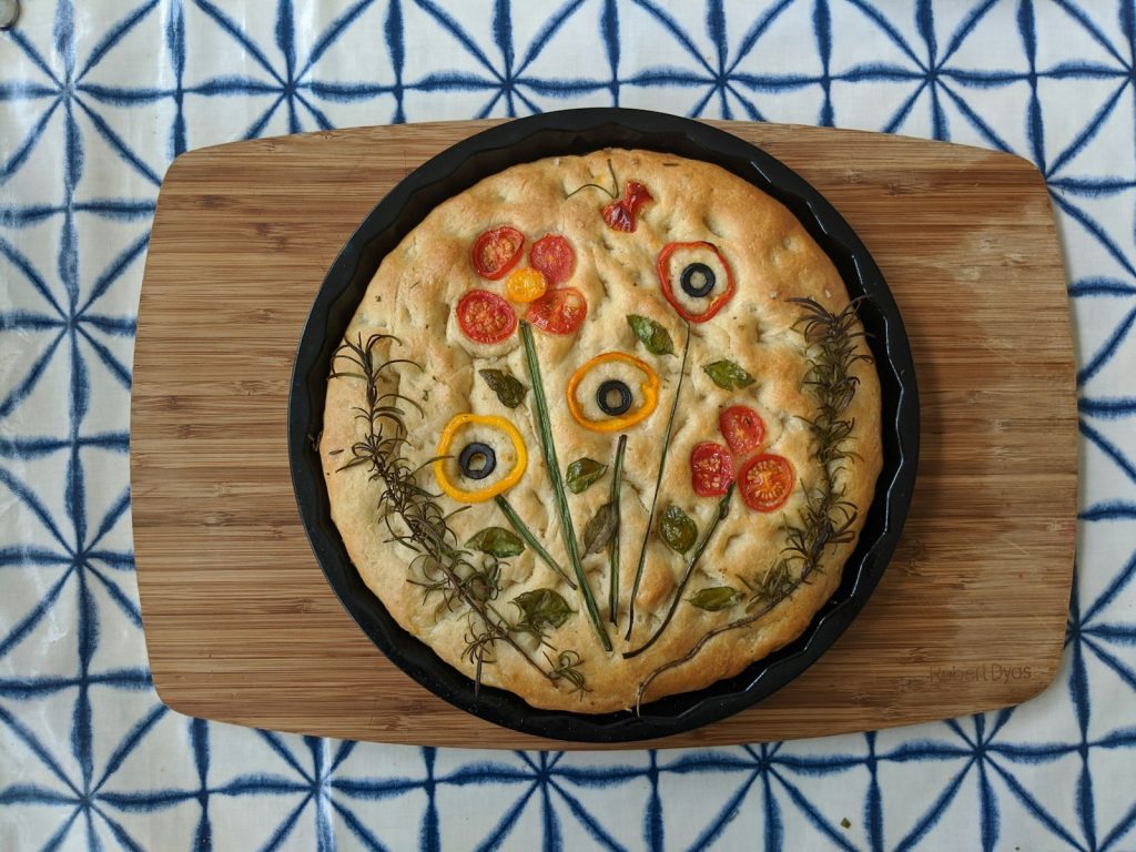 Round focaccia topped with herbs and vegetables