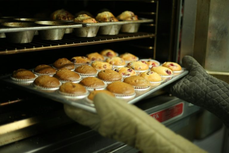 Baker pulling a tray of muffins from the oven